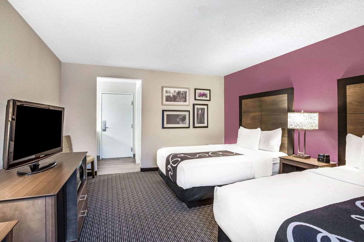 Une chambre d’hôtel avec deux lits, une télévision, un bureau et une porte donnant sur un couloir.