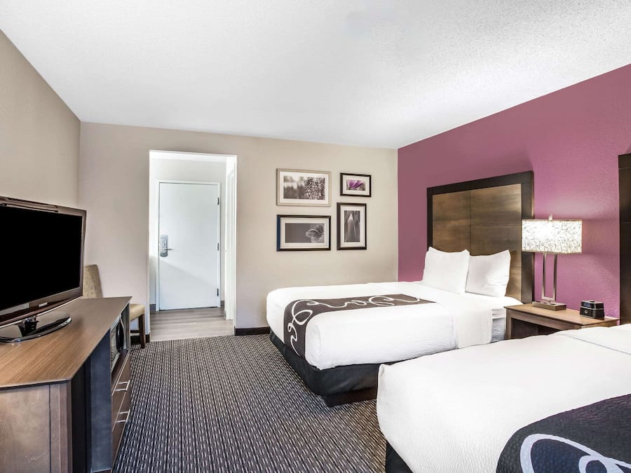 Quarto de hotel com duas camas, televisão, escrivaninha e porta para um corredor.