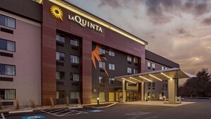 A La Quinta hotel with a modern facade, a large sun logo, and a covered entrance. - La Quinta Inn & Suites by Wyndham Hartford - Bradley Airport (Windsor Locks)