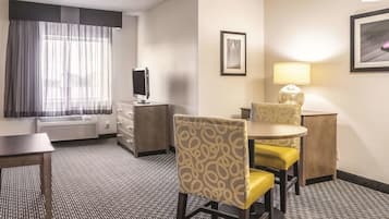 A hotel room with a desk, two chairs, a television, a lamp, and a framed picture on the wall.