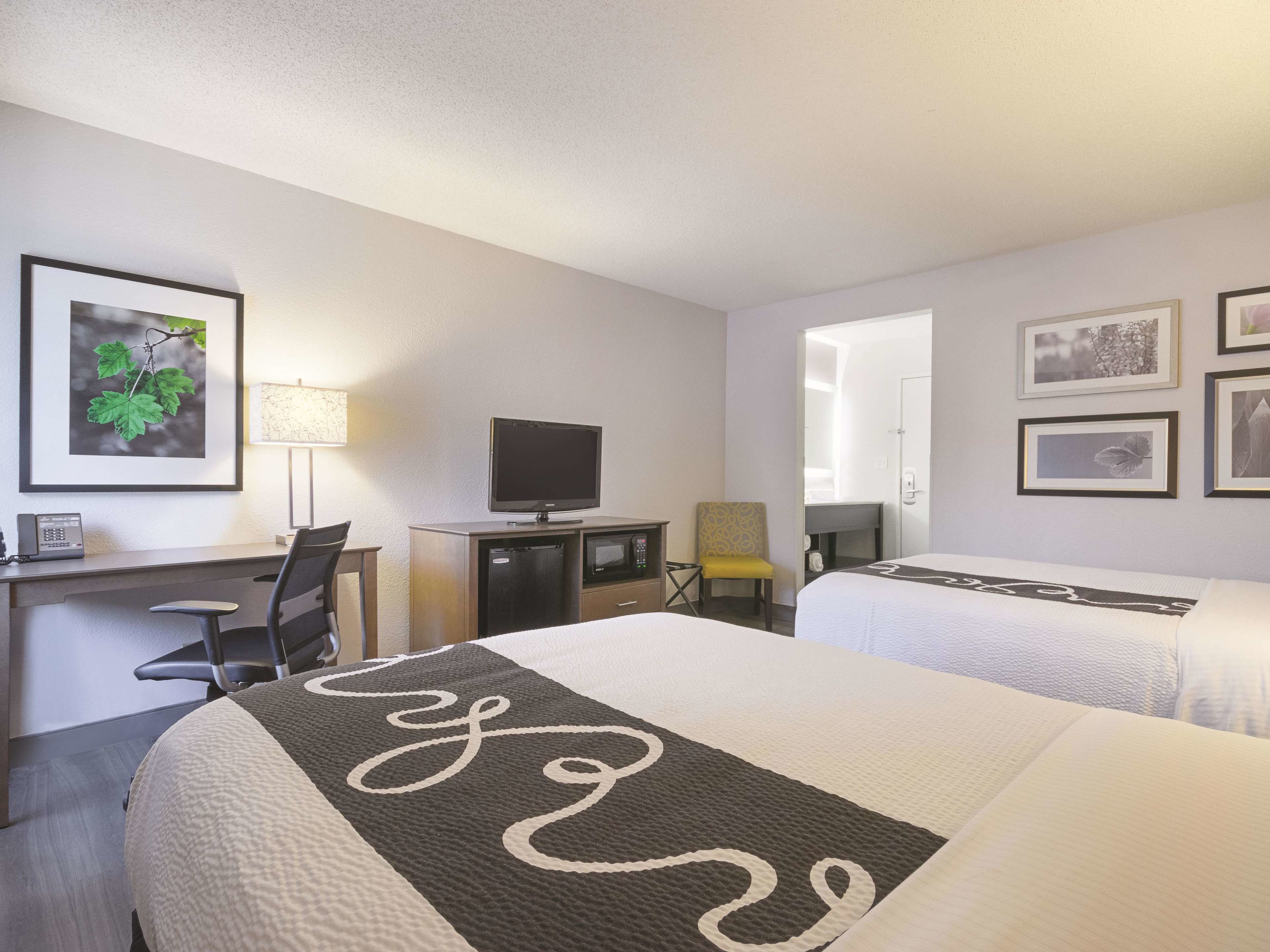 Een hotelkamer met twee bedden, een bureau met een computer, een televisie en ingelijste foto’s aan de muur.