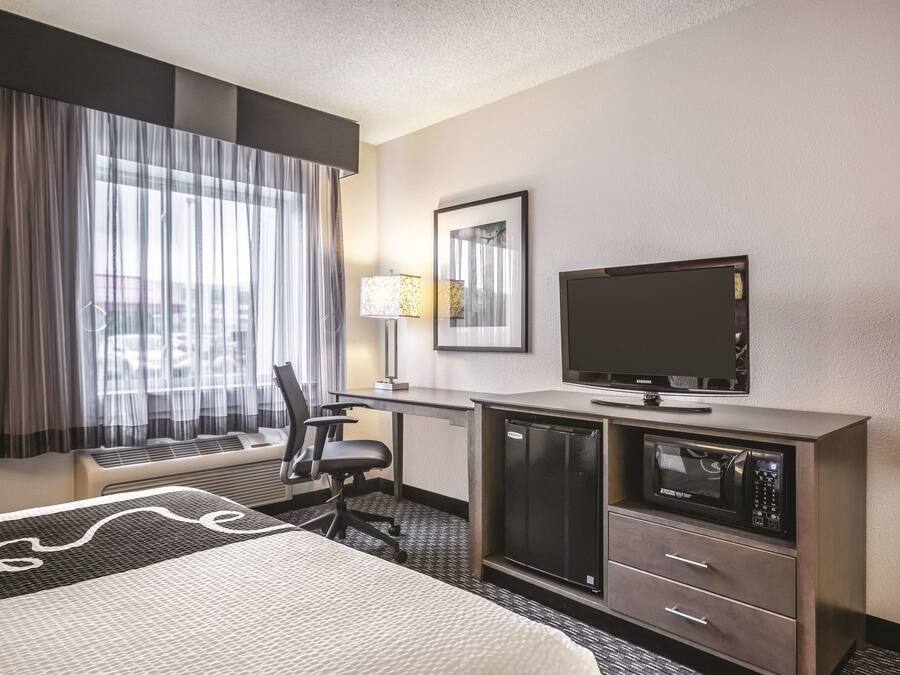 Una habitación de hotel con una cama, un escritorio con televisor, un refrigerador y una silla.