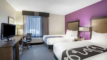 A hotel room with two beds, a desk with a TV, and a window with curtains.