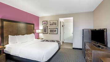 A hotel room with a large bed, a TV, a desk, and a door leading to another room.