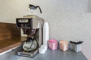 A Bunn coffee machine with disposable cups and a glass carafe, along with containers of coffee creamer and stir sticks. - Knights Inn Peru (Peru)