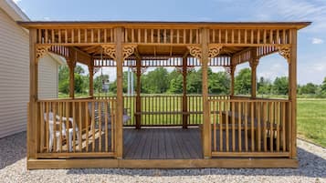 Un belvédère en bois, doté d’un banc et de chaises, entouré d’une zone recouverte de gravier et d’un champ d’herbe.
