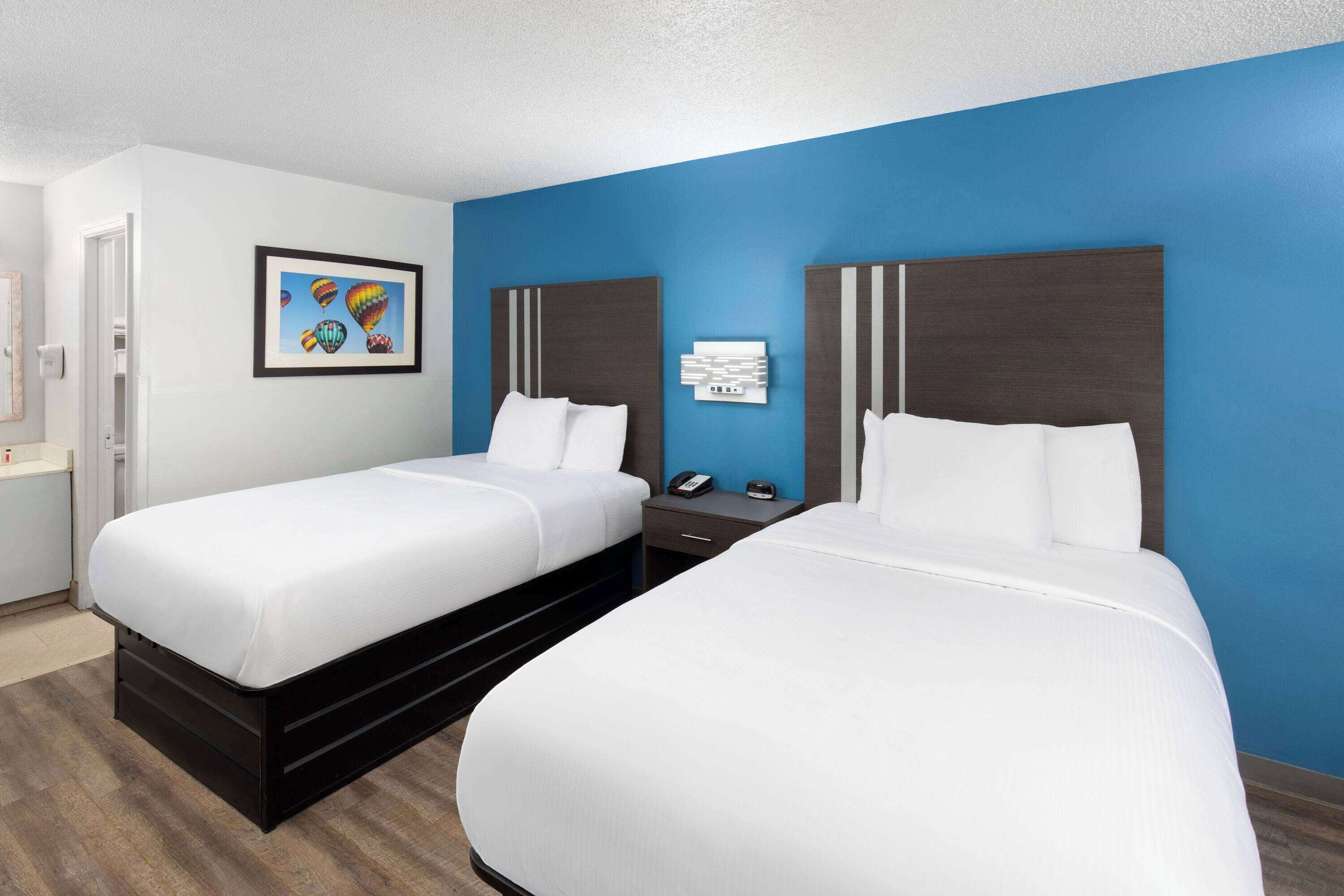 A hotel room with two beds, a nightstand, a framed picture on the wall, and a blue accent wall.