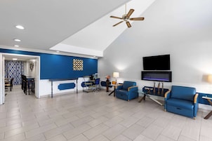 Una sala de estar moderna con una pared azul de acento, un ventilador de techo, un televisor de pantalla plana y una zona de comedor con sillas y una mesa.