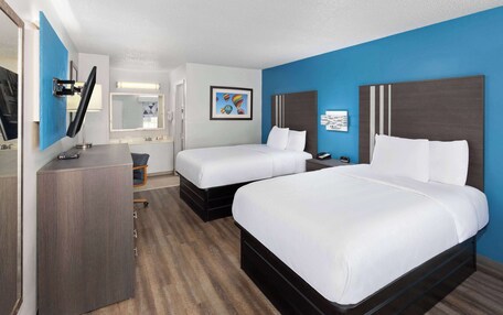 A hotel room with two beds, a desk, a chair, and a mirror.