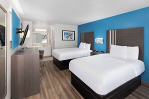 A hotel room with two beds, a desk, a chair, and a mirror.