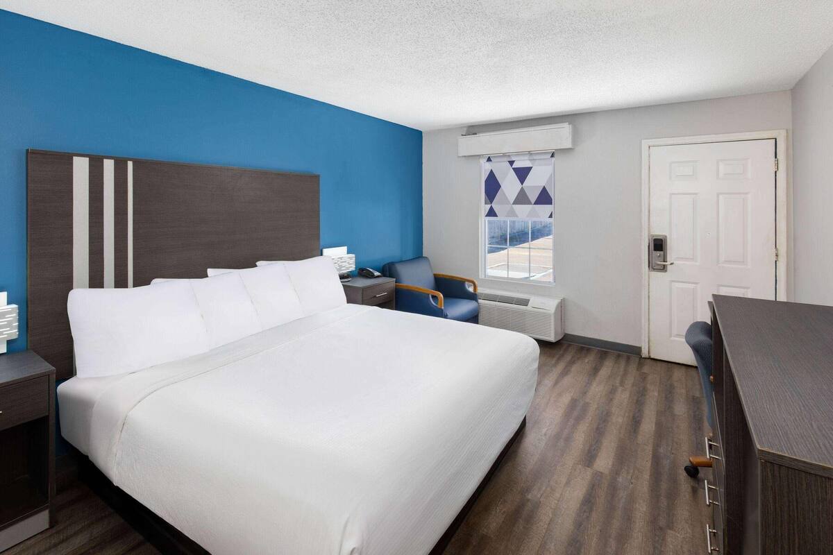 Une chambre d’hôtel avec un grand lit, un bureau, une chaise, une fenêtre donnant sur un beau paysage et une porte.