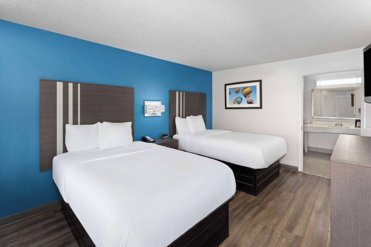 Une chambre d’hôtel avec deux lits, un grand miroir, un bureau et un mur d’accent bleu.