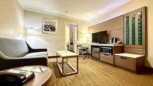 A hotel room with a sofa, a desk with a telephone, a chair, a television, a microwave, and a cabinet with decorative panels.