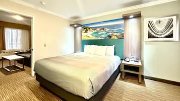 A hotel room with a large bed, a desk, a chair, a mirror, and a painting of a coastal scene.