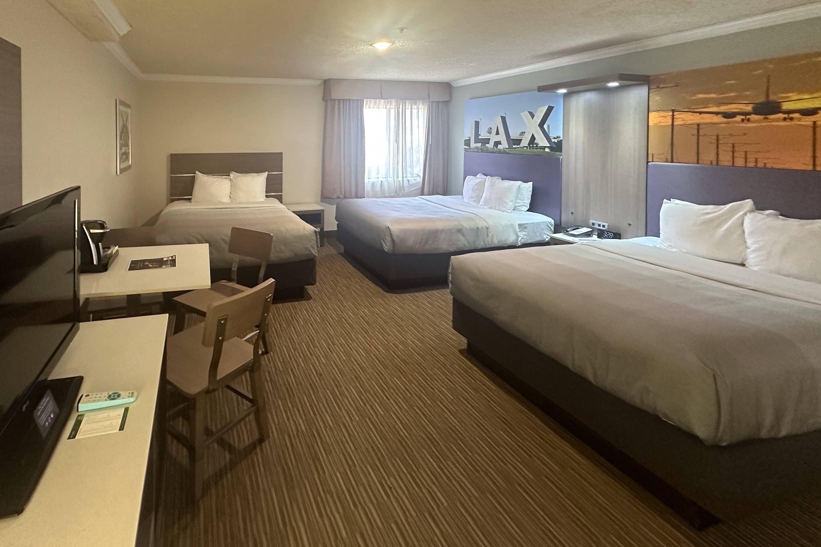 Habitación de hotel con dos camas, un escritorio con televisor y una silla.