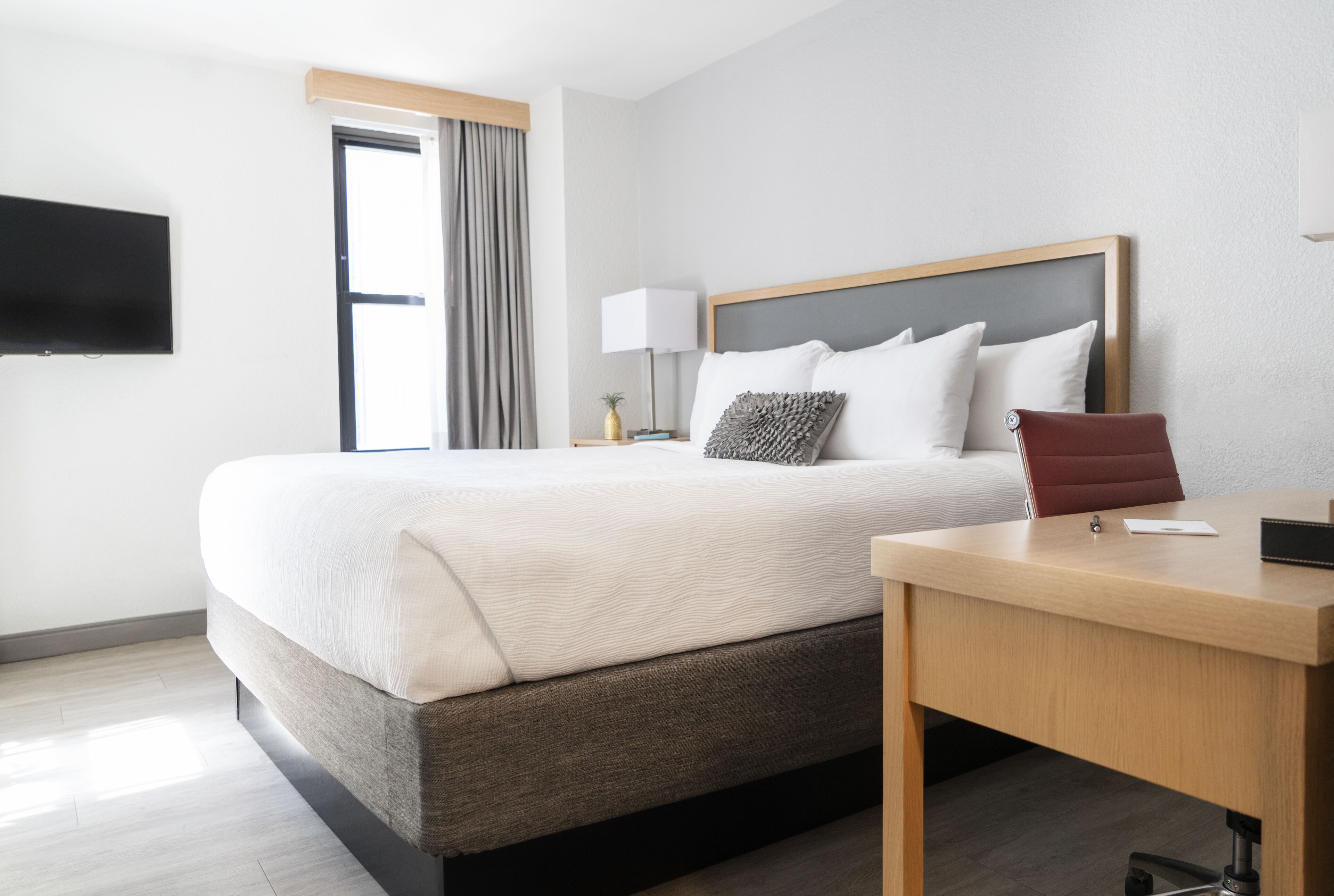 Et moderne hotelværelse med en stor seng, et skrivebord, et fladskærms-tv og et vindue med gardiner.
