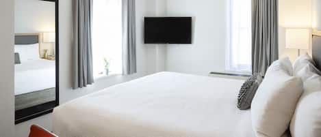 A hotel room with a large bed, a flat-screen TV mounted on the wall, and a window with curtains.