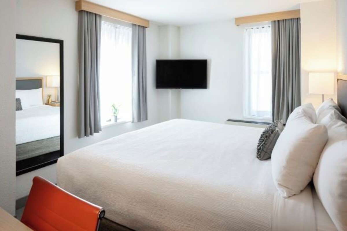 Quarto de hotel com uma cama grande, televisão de tela plana na parede e uma janela com cortinas.