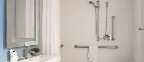 A bathroom with a sink, mirror, shower, and towel rack.