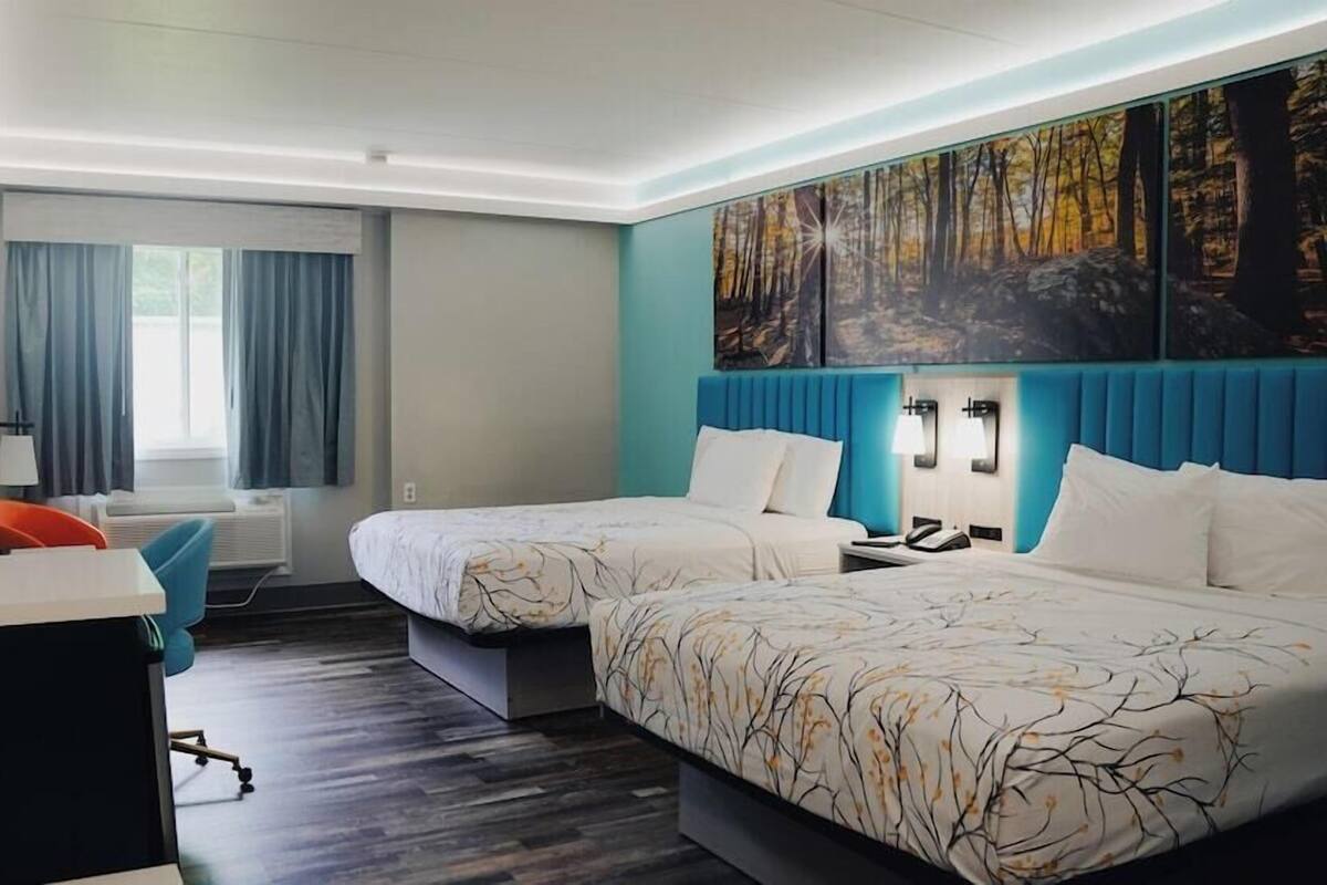 A hotel room with two beds, a desk, a chair, a TV, and a painting on the wall.