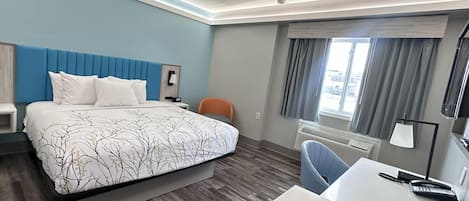 A hotel room with a bed, a desk, a chair, a nightstand, and a window with curtains.