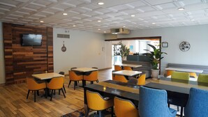 Un restaurant moderne avec des murs lambrissés, un téléviseur à écran plat et différents types de sièges, notamment des tables et des banquettes.