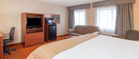A hotel room with a large bed, a desk with a television, a chair, and a small cabinet.