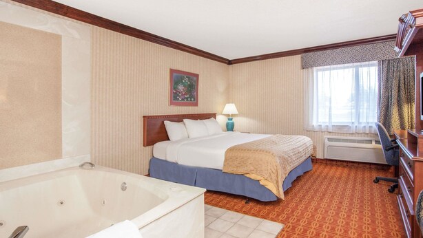 A hotel room with a large bed, a separate bathroom with a bathtub, a desk, and a window with curtains.