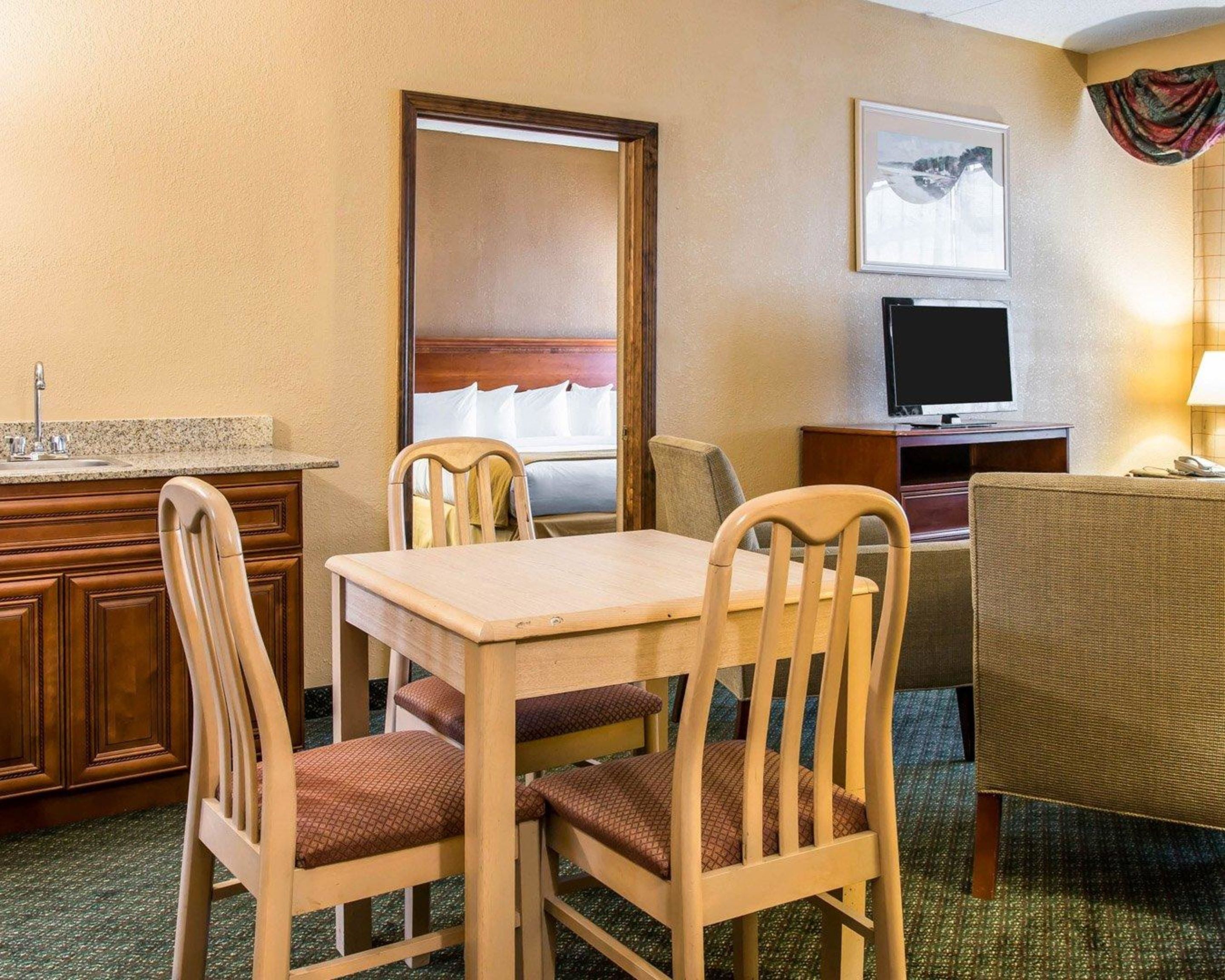 Hotelkamer met een eettafel, twee stoelen, een televisie, een bed en een zichtbare badkamer door een geopende deur.
