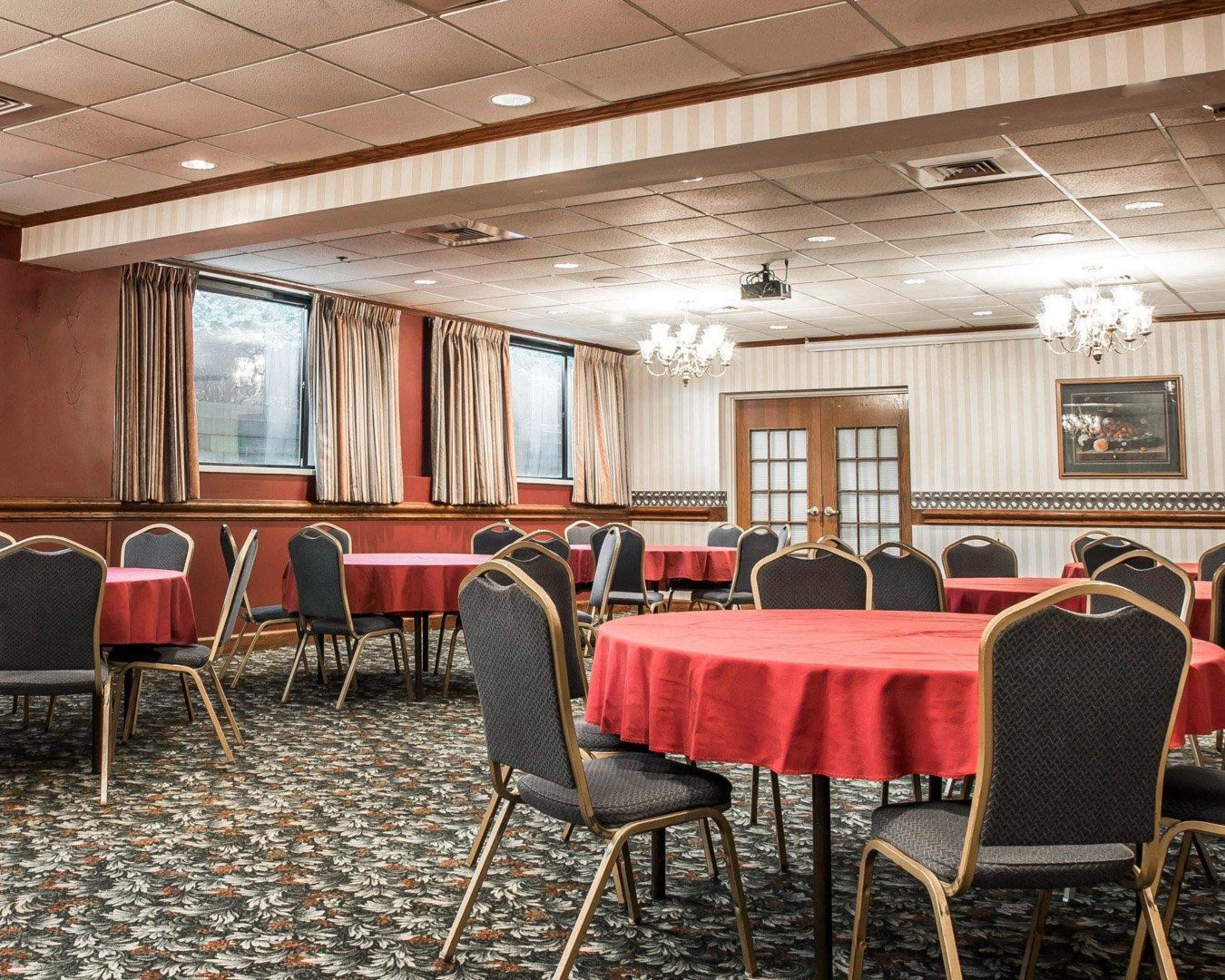 A conference room with tables and chairs, large windows with curtains, a chandelier, and a patterned carpet.