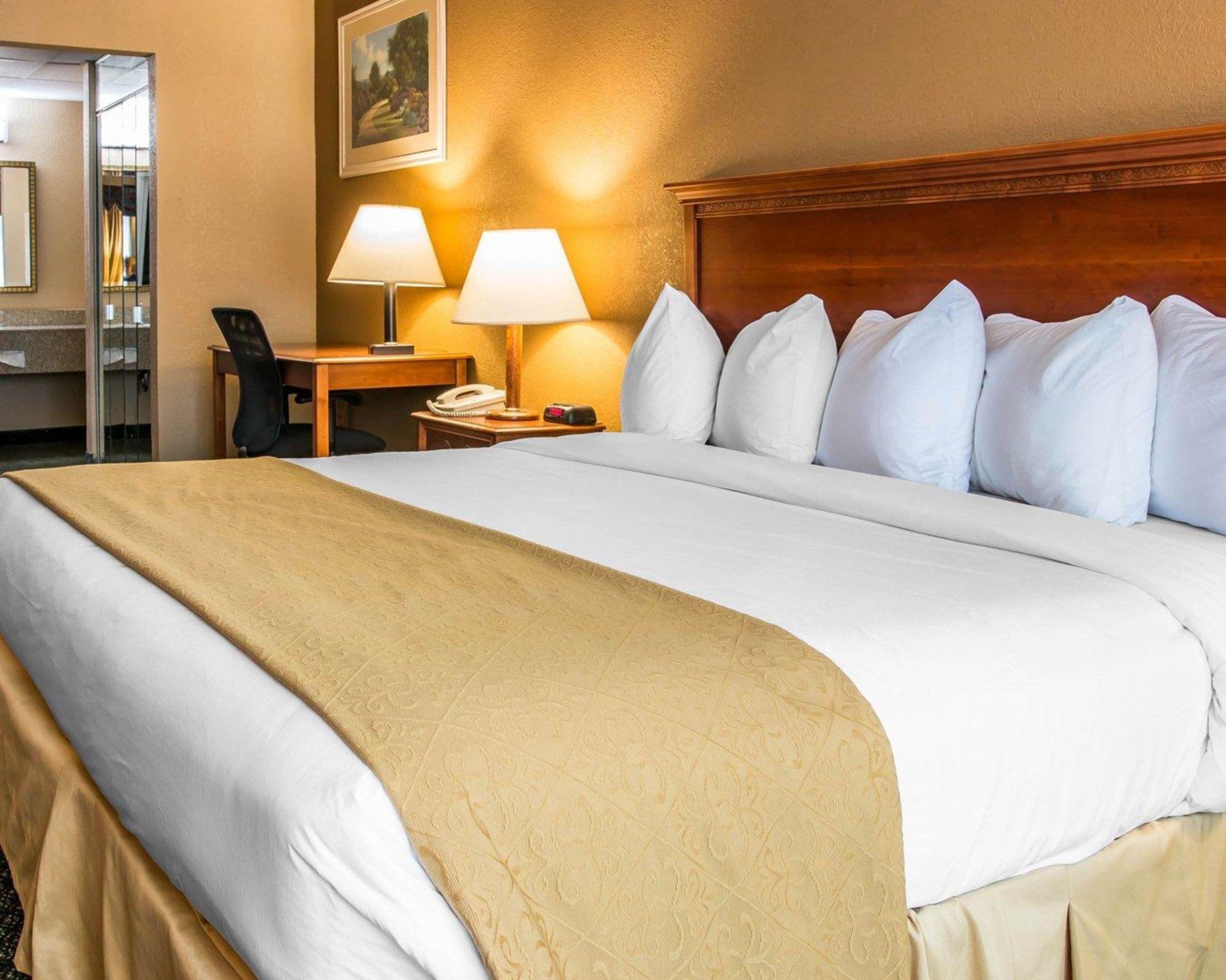 Een hotelkamer met een groot bed, twee bedlampen, een houten hoofdeinde, een bureau met telefoon en een spiegel.