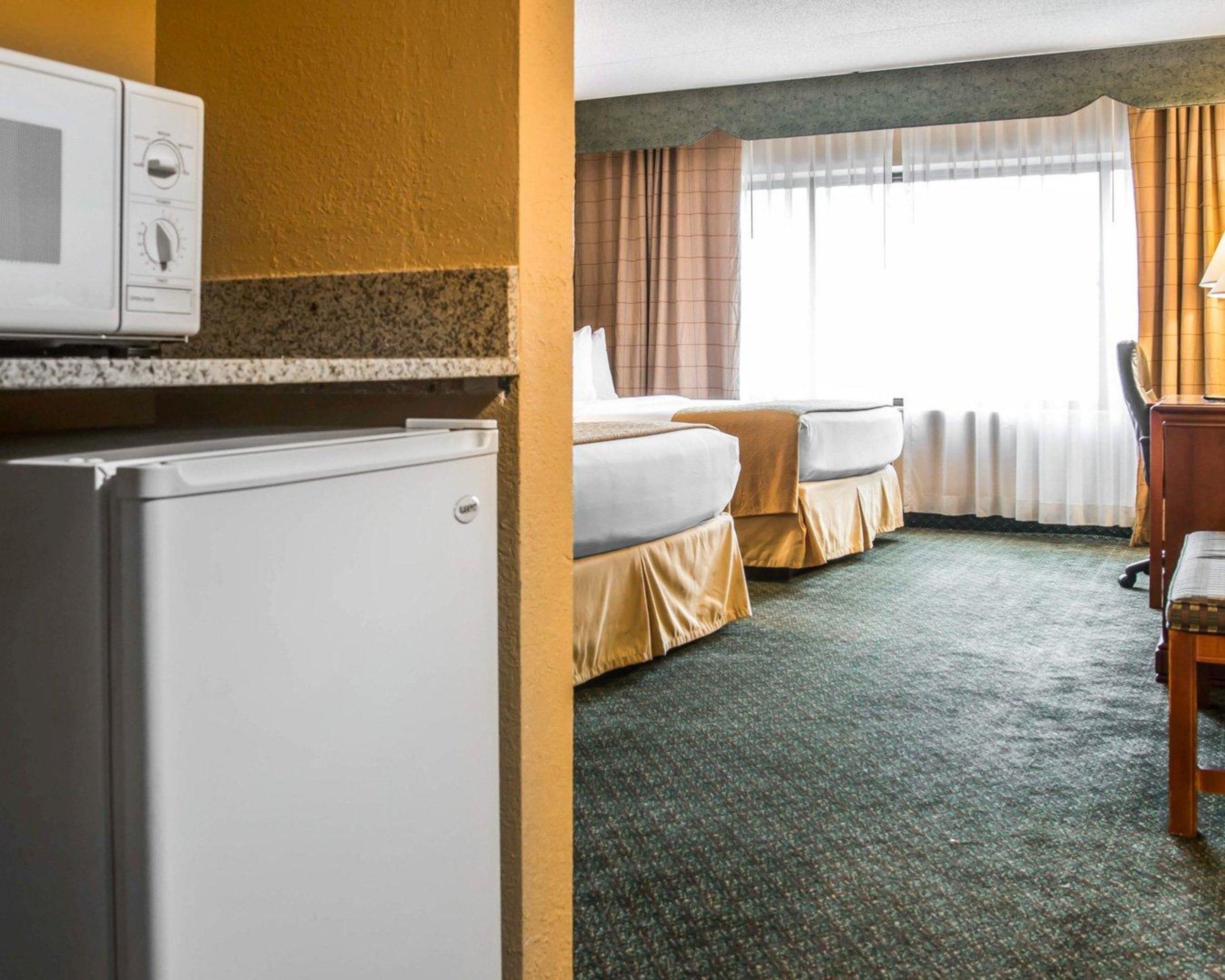A hotel room with two beds, a refrigerator, a desk, and a window with curtains.