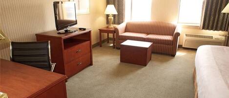 Een hotelkamer met een bureau, televisie, bank en bed.