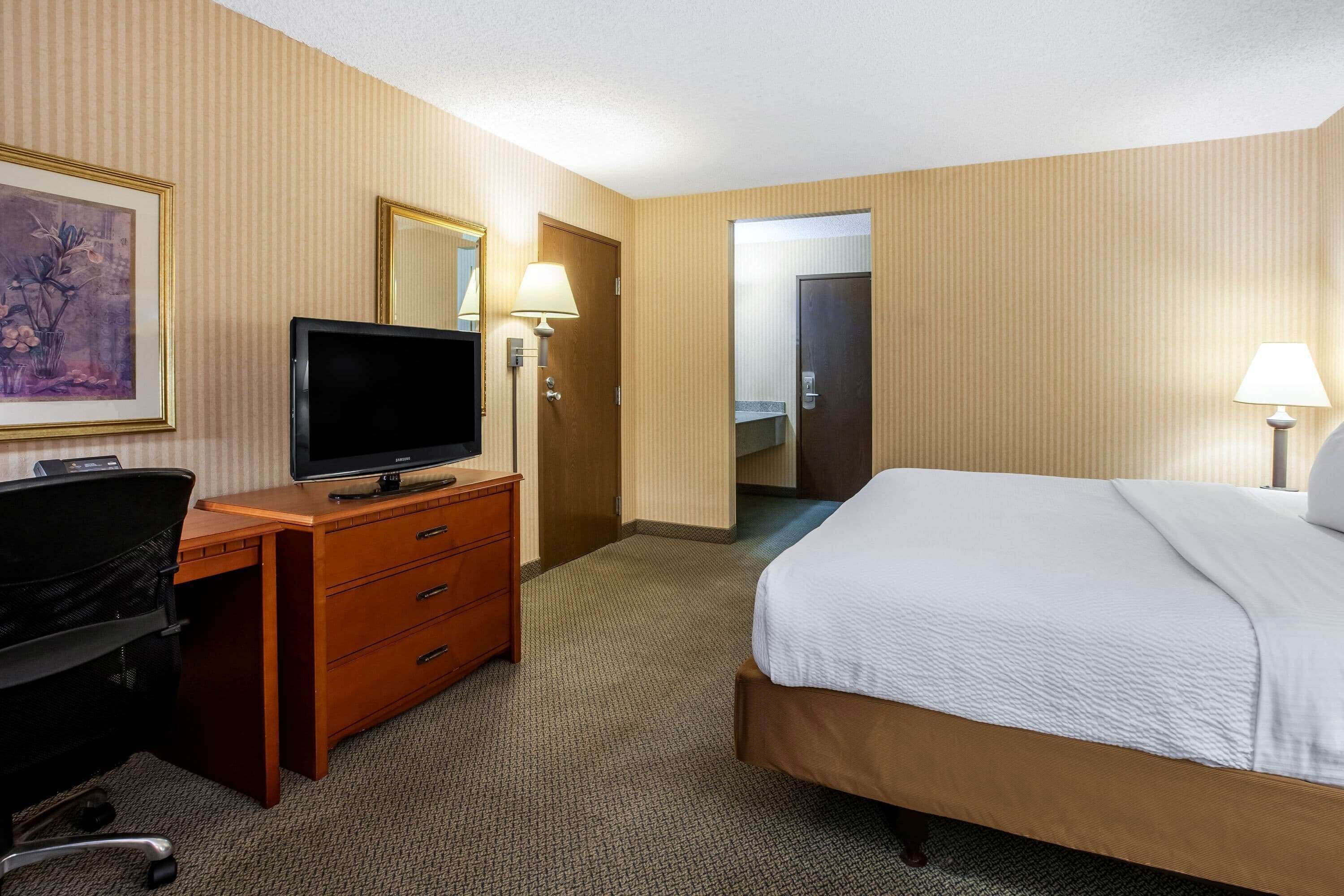 Una habitación de hotel con una cama, un escritorio con televisor, una cómoda y dos lámparas.
