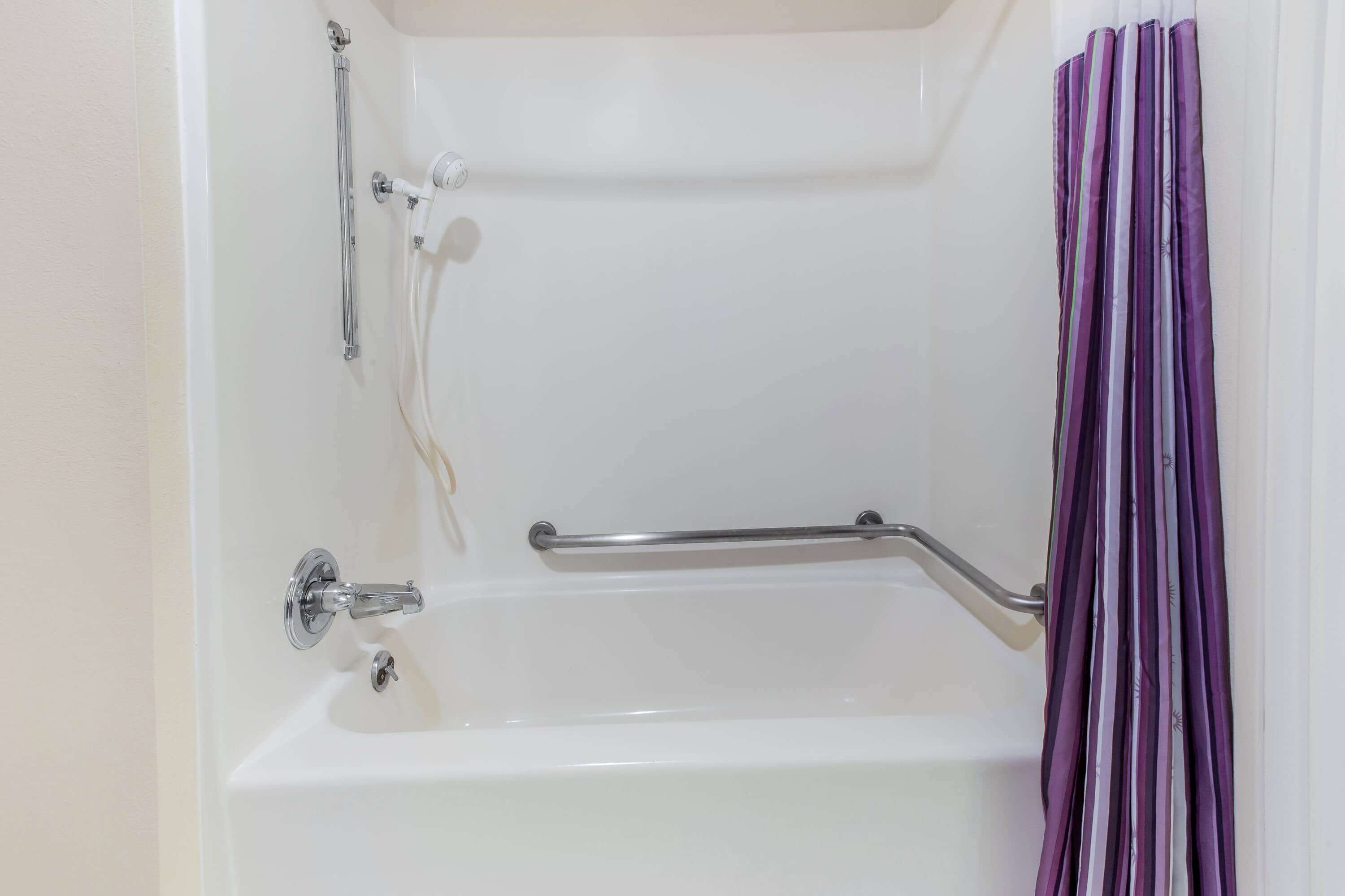A bathtub with a grab bar, a showerhead, and a curtain.