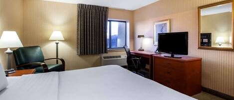 Habitación de hotel con una cama grande, un escritorio con televisor, una silla y una ventana con cortinas.