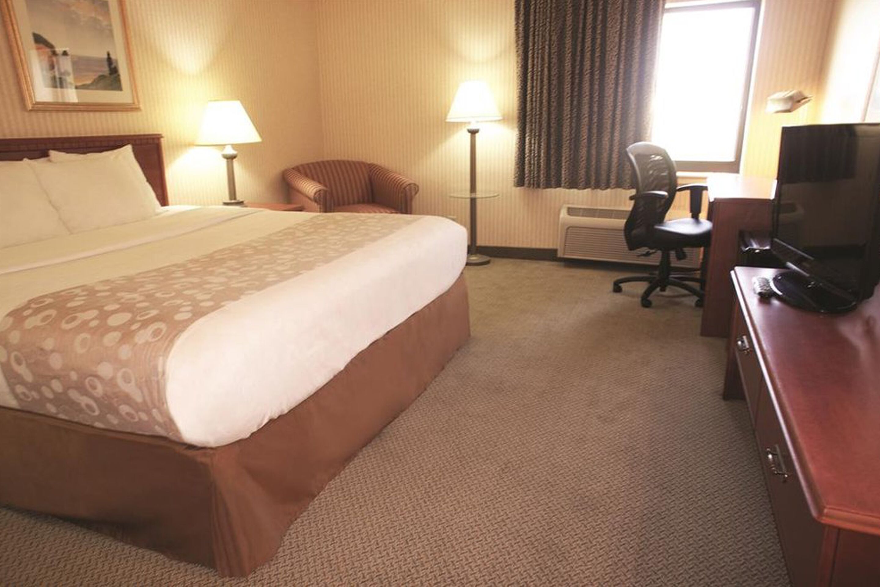 A hotel room with a large bed, a desk with a computer, a chair, and a television.