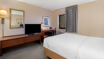 A hotel room with a bed, a desk, a TV, a lamp, and a window with curtains.