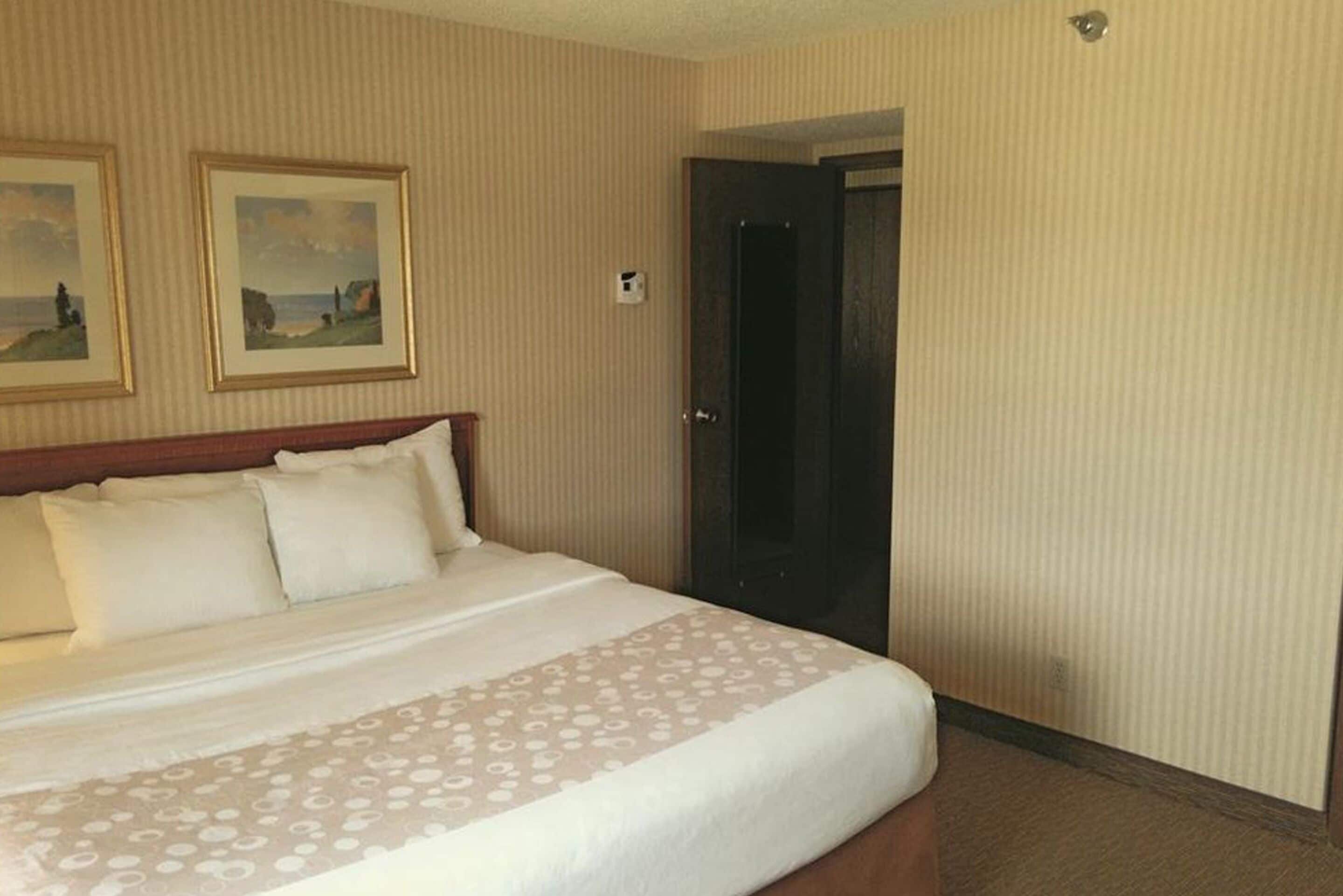 A hotel room with a large bed, a wooden headboard, two framed pictures on the wall, and a door to the right.