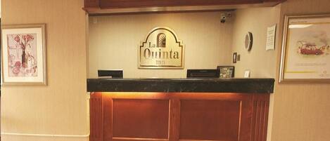 Una mesa de recepción con un letrero que dice "La Quinta Inn" y un tapete verde con el mismo nombre.