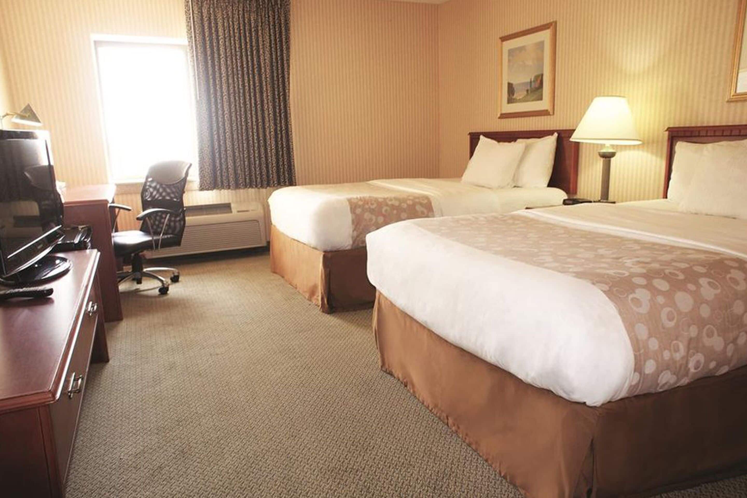 A hotel room with two beds, a desk, a chair, and a television.