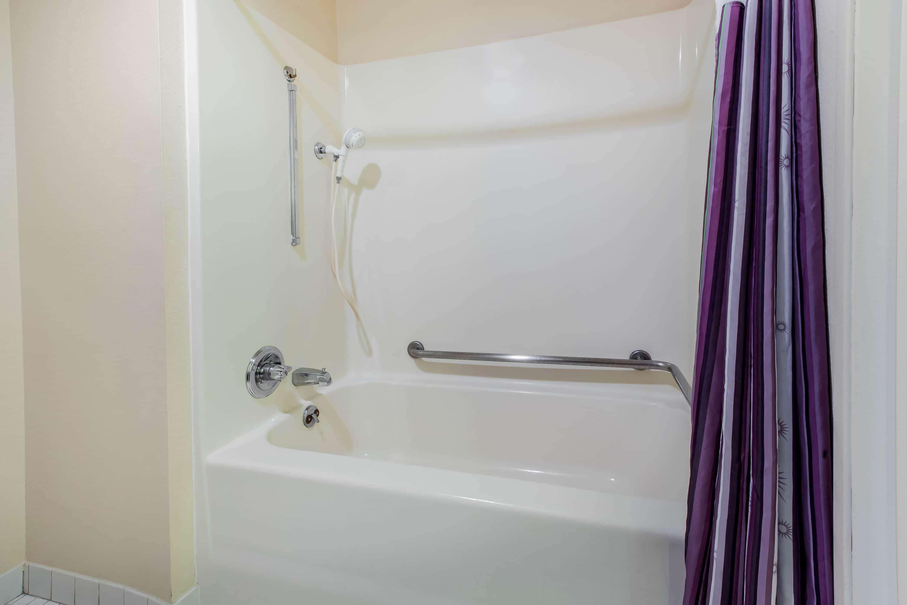 A bathtub with a showerhead, grab bar, and a purple striped shower curtain.