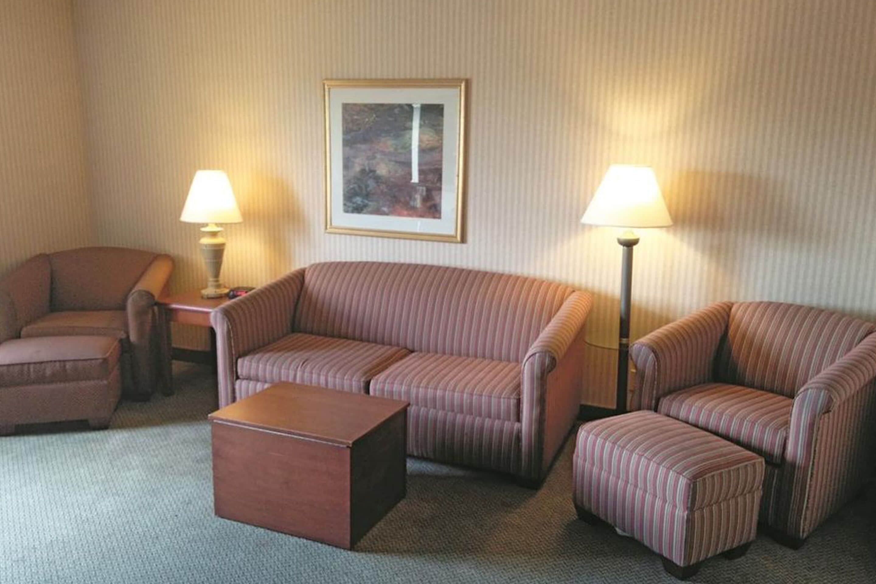 A hotel room with a striped sofa set, a wooden coffee table, and two lamps.