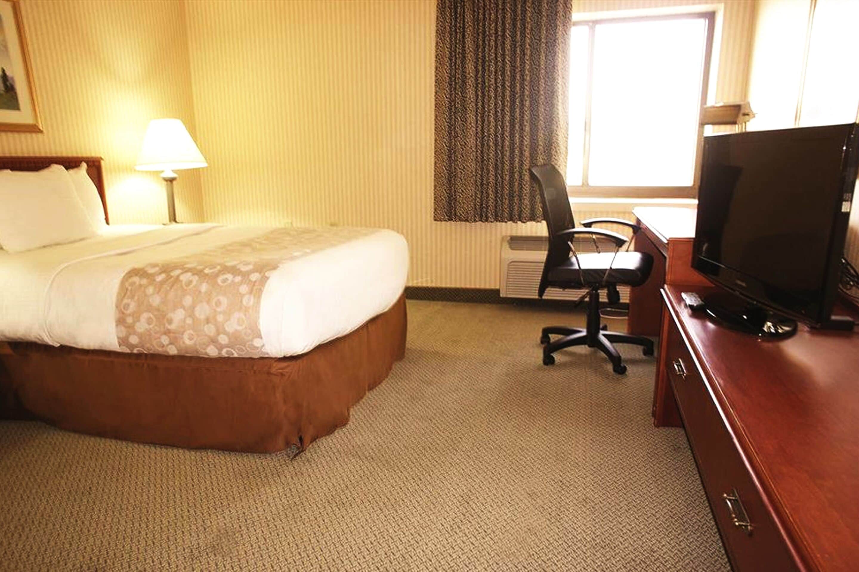 Una habitación de hotel con cama, escritorio con televisor, silla y ventana con cortinas.