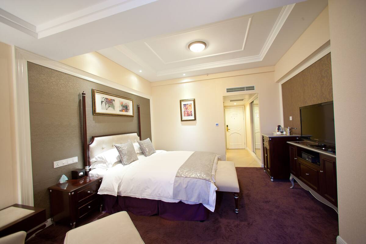 Une chambre d’hôtel avec un grand lit, une table de chevet, une commode et un téléviseur.