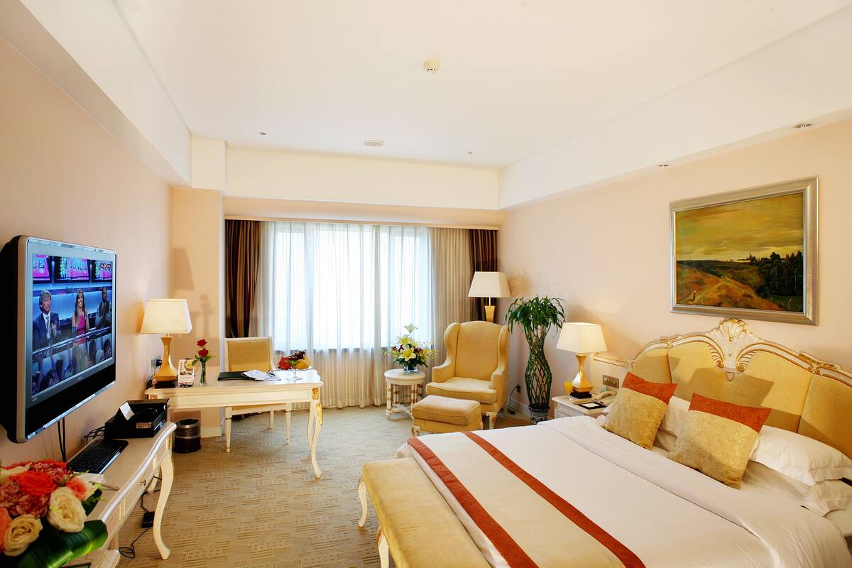 Une chambre d’hôtel avec un grand lit, un bureau avec un ordinateur, une télévision et une chaise.