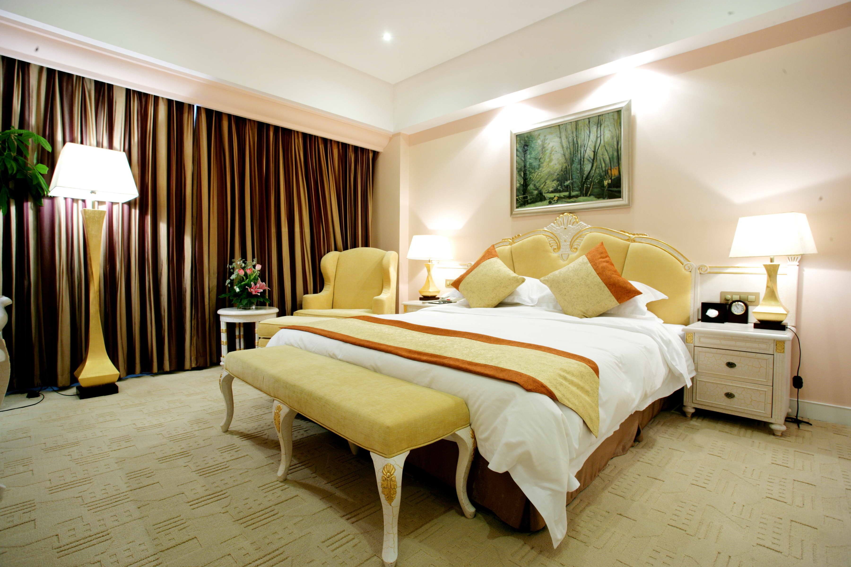 A hotel room with a large bed, bedside tables, a bench, a painting on the wall, and curtains.
