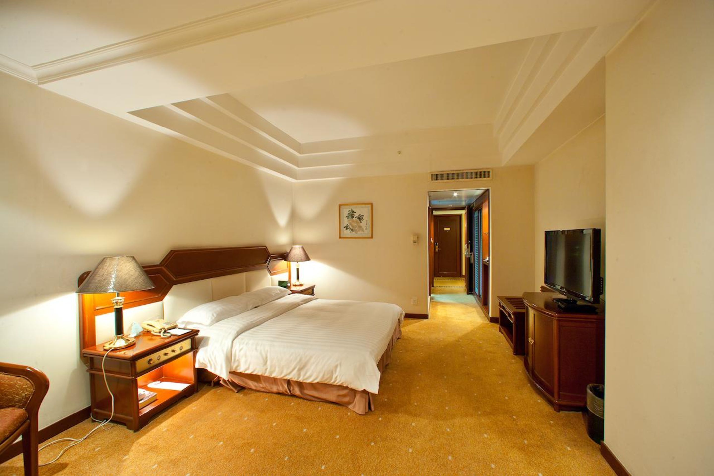 Ein Hotelzimmer mit einem großen Bett, Nachttischen mit Lampen, einem Fernseher und Teppichboden.
