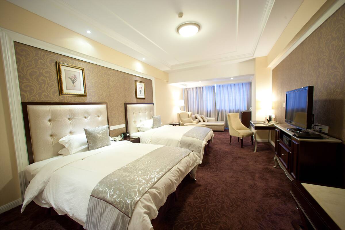 Une chambre d’hôtel avec deux lits, un bureau, une télévision et une fenêtre avec des rideaux.