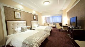 A hotel room with two beds, a desk, a television, and a window with curtains.